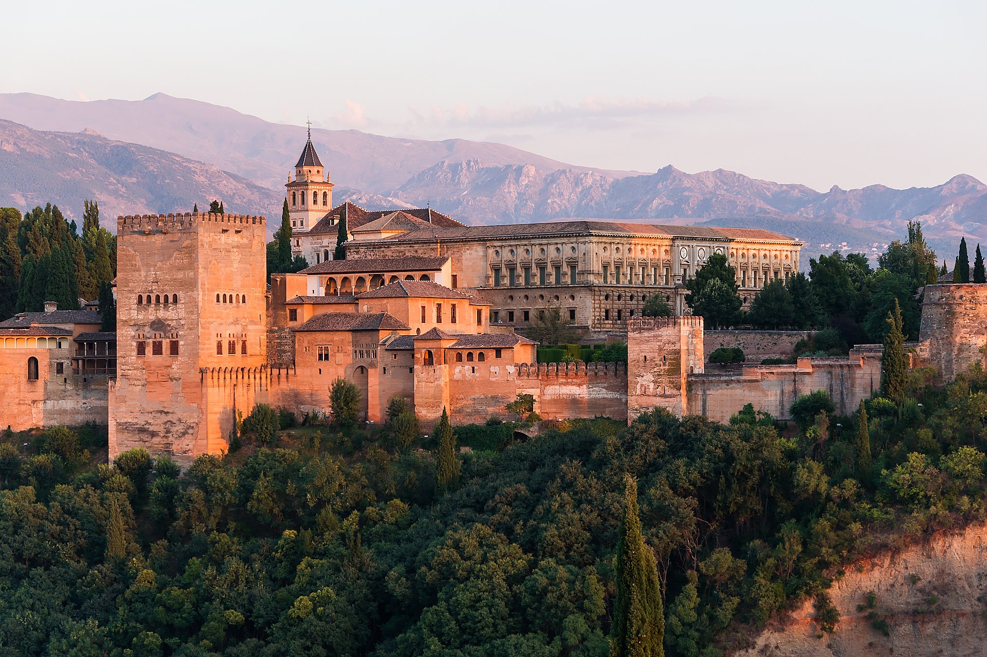 Alhambra al amanecer: murallas, torres nazaríes y el palacio de Carlos V de planta cuadrada, Sierra Nevada al fondo.